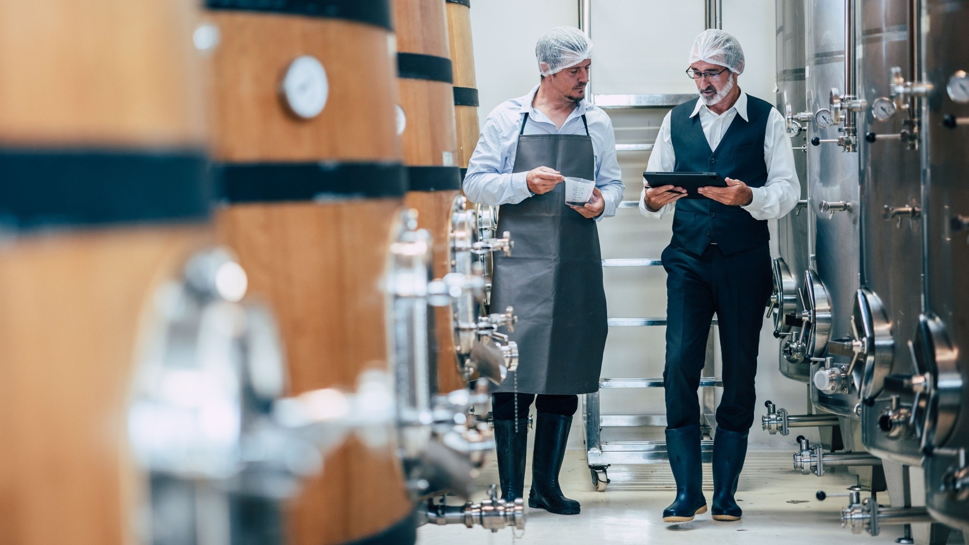 two men stood in a brewery with barrels of alcohol in the frame