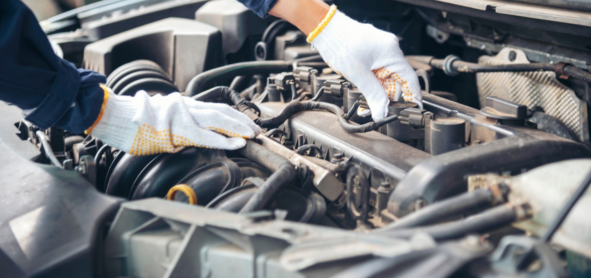 Man working on a car engine as a mechanic with white stained gloves on 