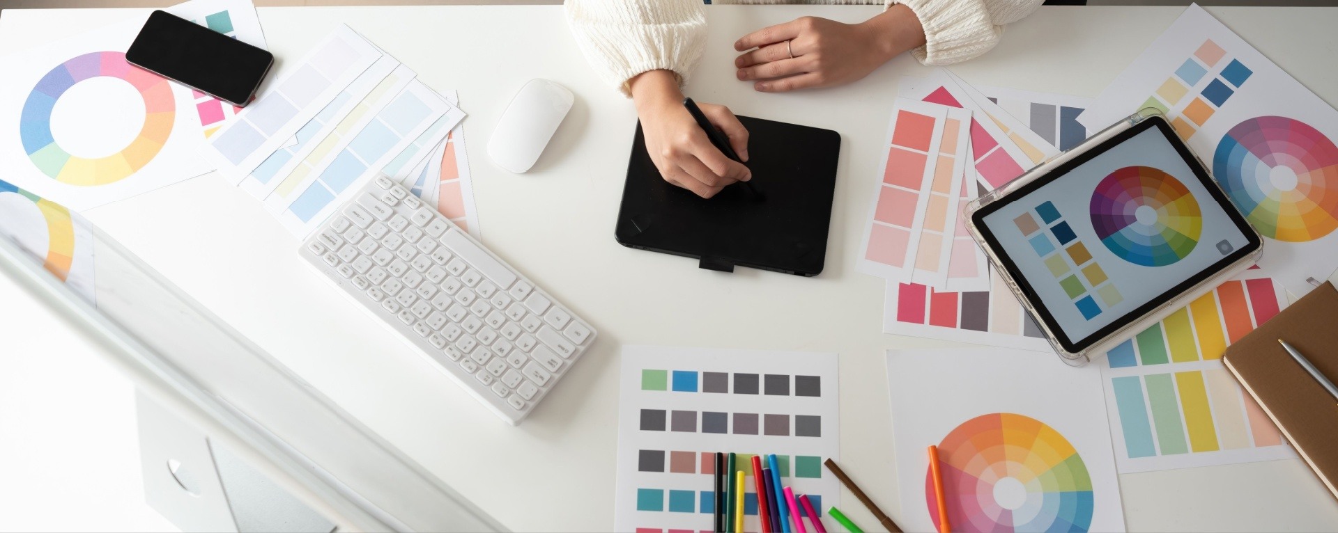 Woman designing on a tablet with lots of design equipment scattered around her 