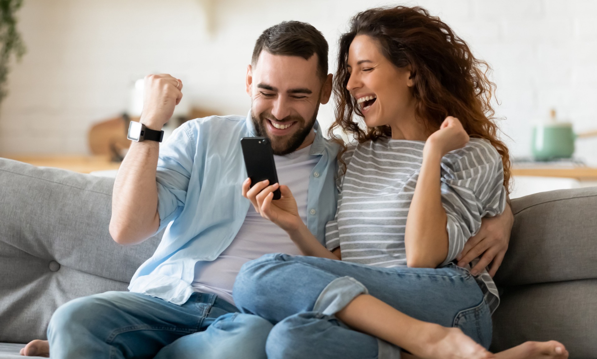 Young couple on their smartphone celebrating their matched betting side hustle win. 