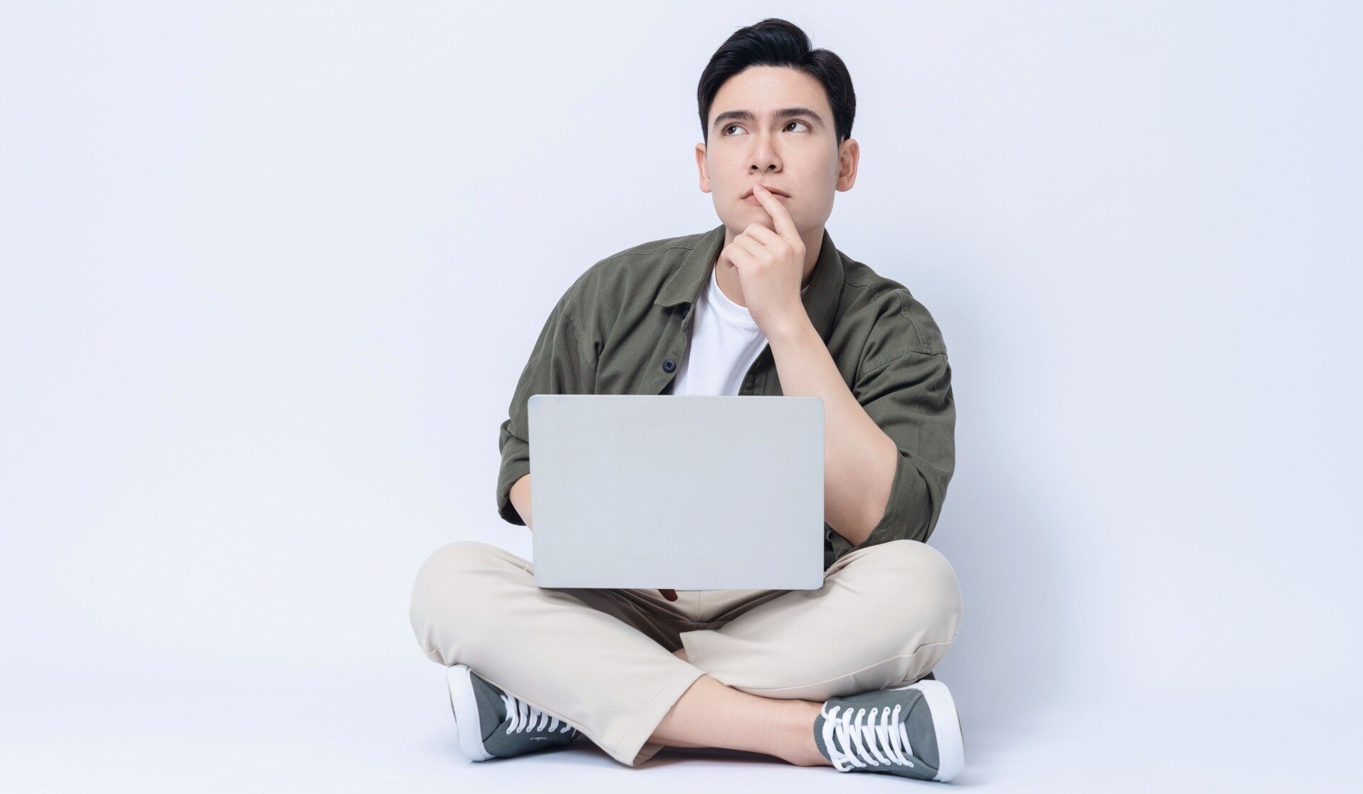 Man with laptop sitting down and looking up curiously