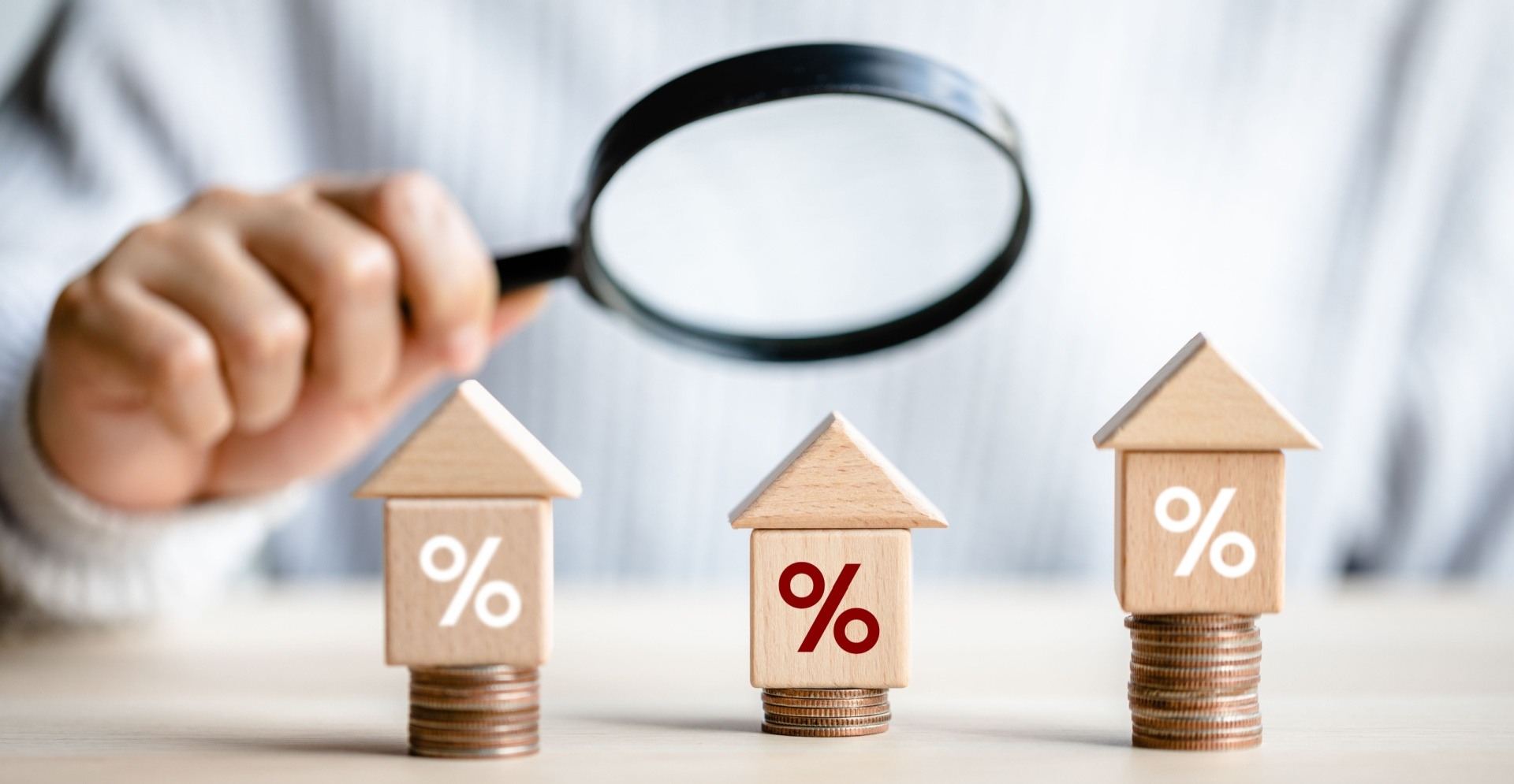 Man holding magnifying glass looking at potential investments represented by small houses on some change.