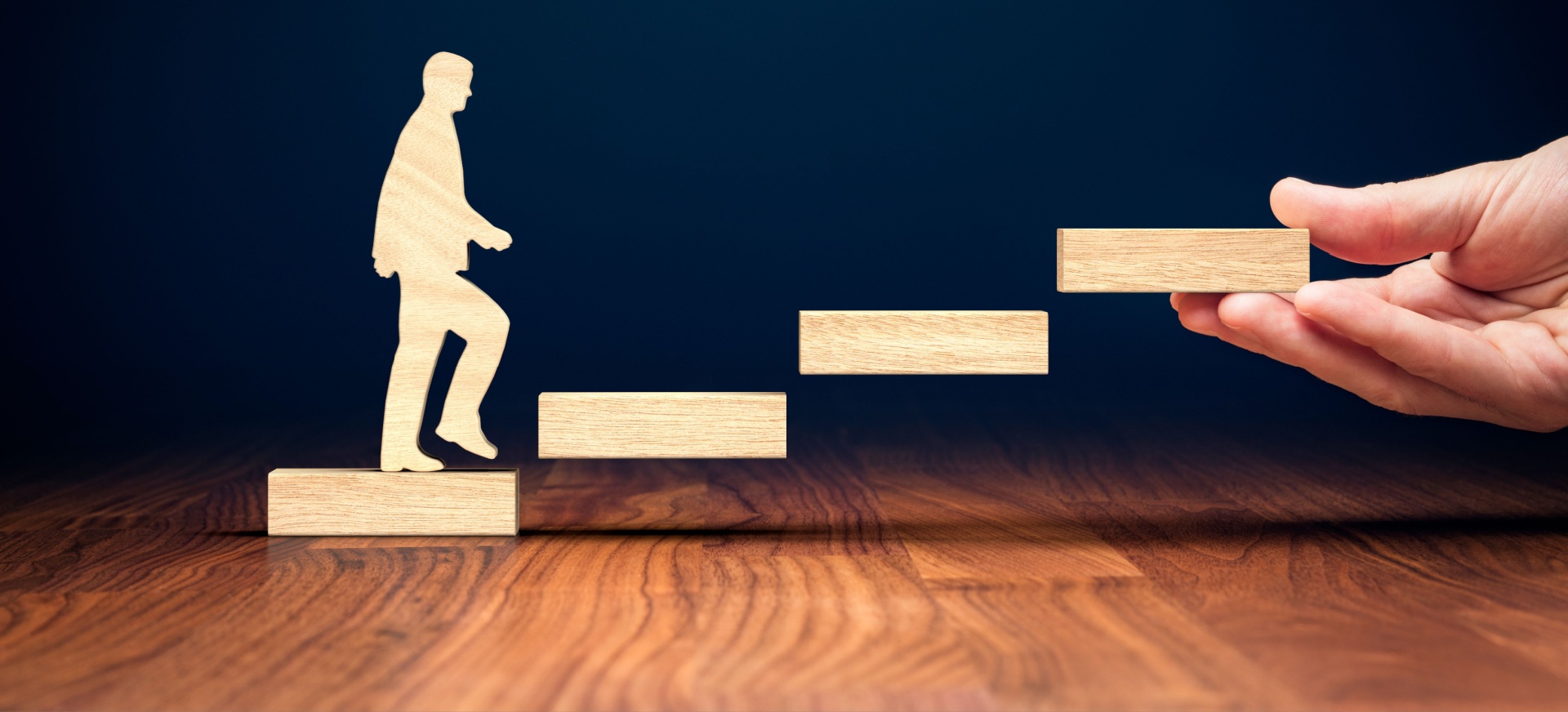 Wooden man taking steps up, with hand holding the wooden bricks. 