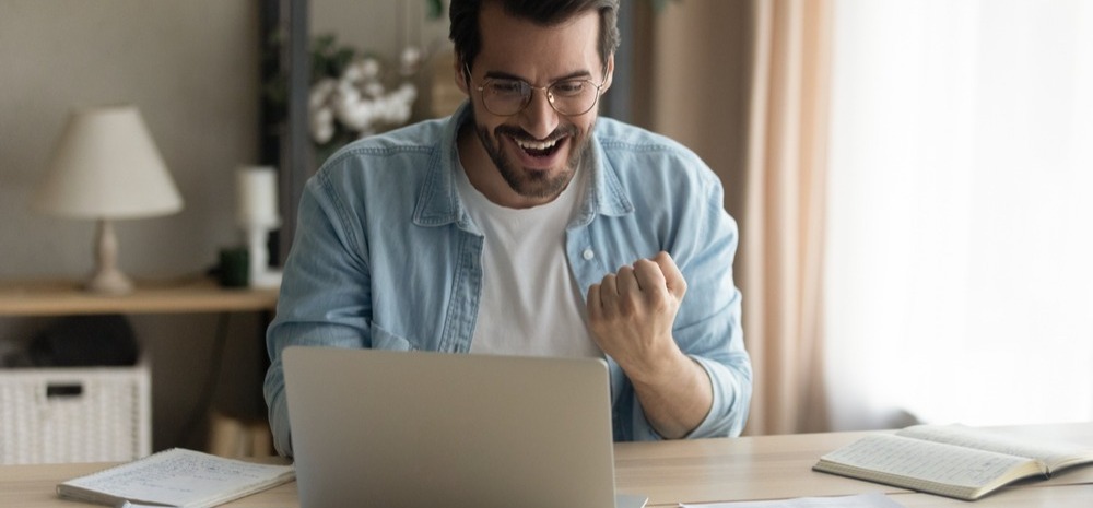Man smiling at his laptop in celebration