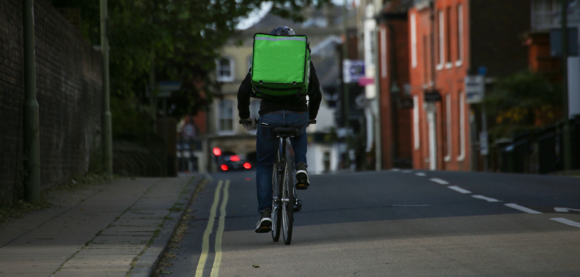 Delivery man rising a bike with a bag on his back down a street.