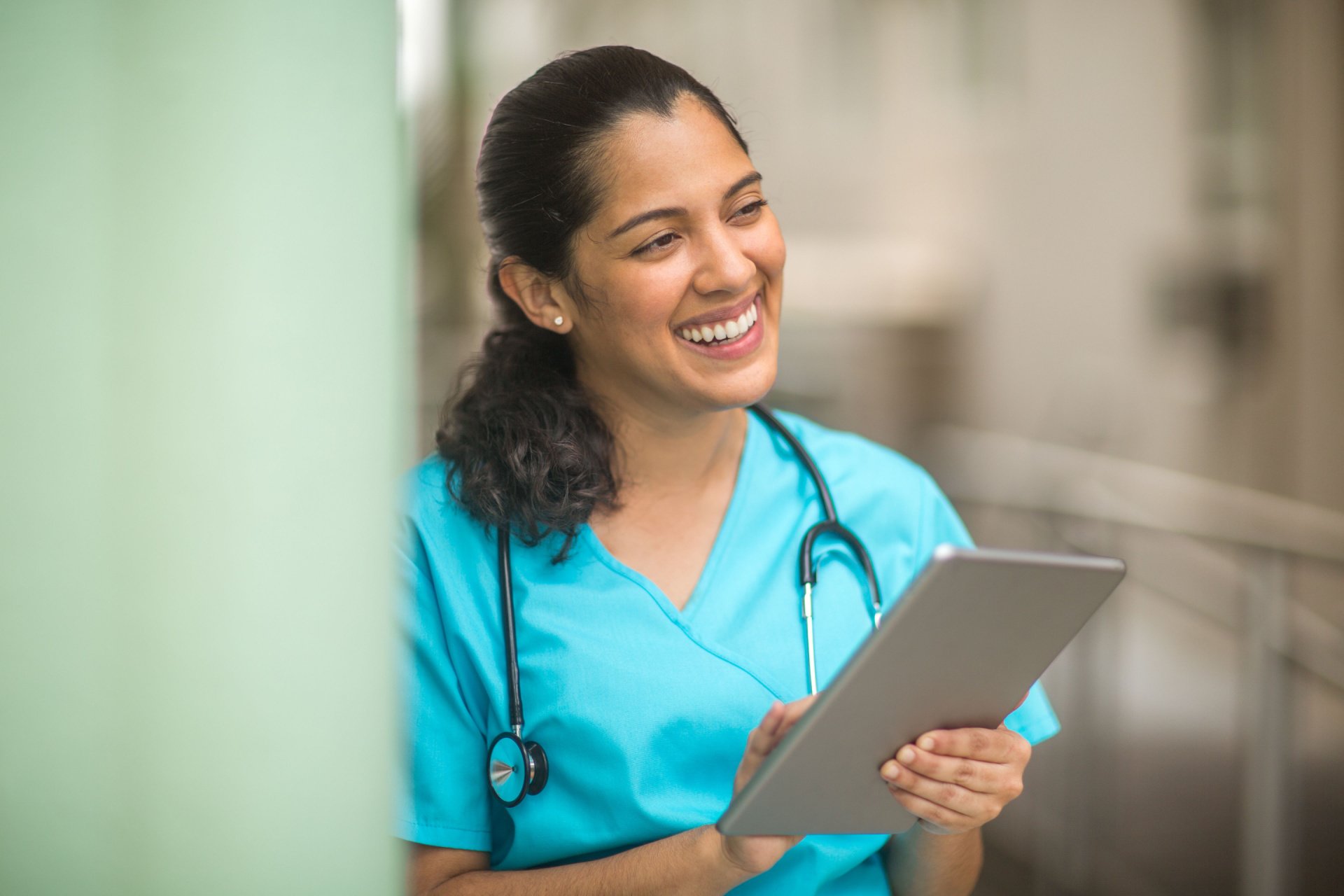 A nurse in a light blue outfit smiling whilst holding a grey clipboard