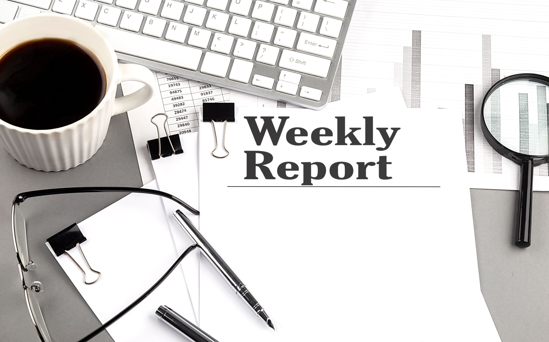 Weekly report on a clutered desk with coffee and a keyboard on there. 
