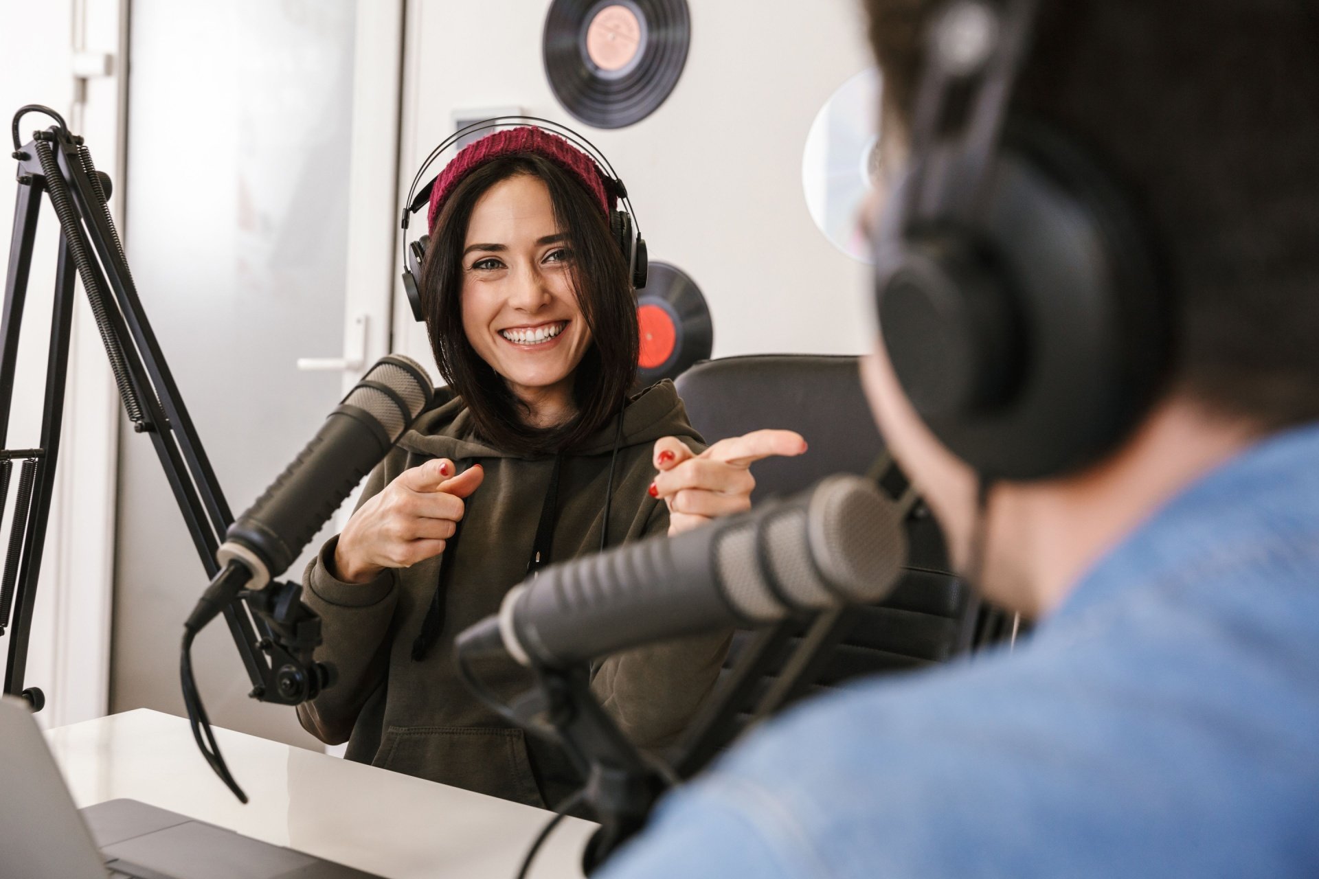 Woman with hood up talking into a mic with another man talking into a mic. 